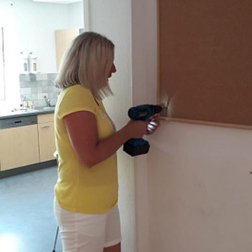 Christine entfernt die Pinwand mit einem Akkuschrauber von der Wand