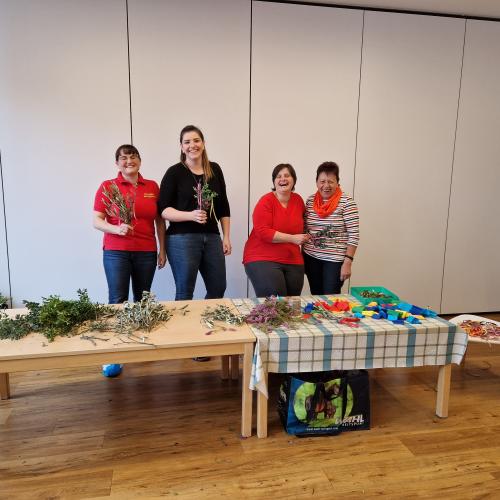 Vier Frauen der Pollinger Bäuerinnen hinter einer Tafel mit Utensilien zum Palmbuschen binden
