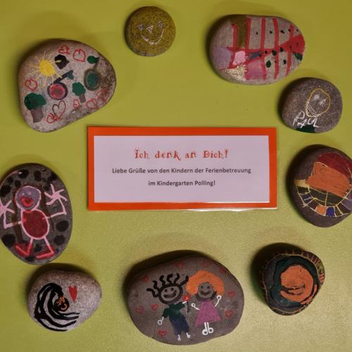 Viele bemalte Steine in einem Kreis liegend mit einem "Liebe Grüße aus dem Kindergarten-Zettel"-auf dem