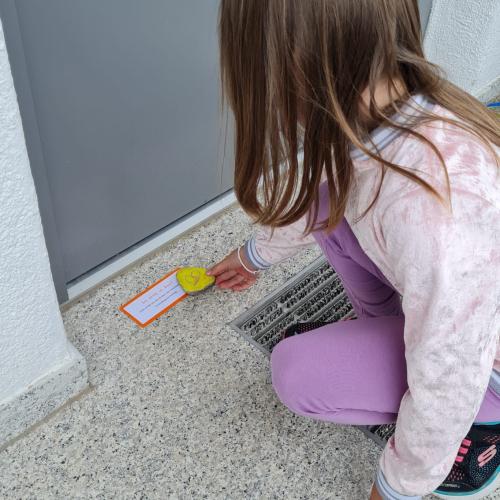 Ein Mädchen legt den bemalten Stein samt einem Zettel mit lieben Grüßen aus dem Kindergarten vor eine Eingangstüre