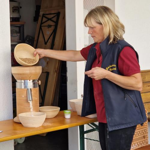 Theresia  Venier schüttet Getreidekörner in die Mühle und  Mehl fällt in die Schüssel