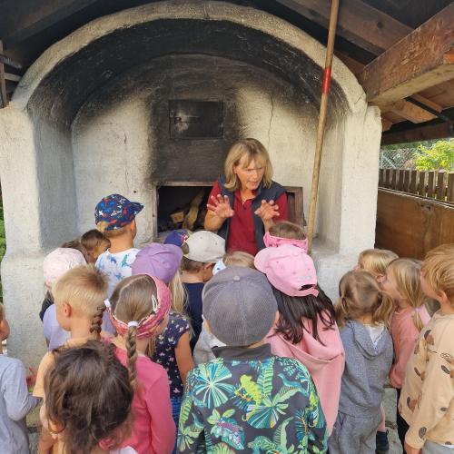 Die Bäuerin erklärt den Kindern vor dem Brotbackofen wie viele Brote Platz haben