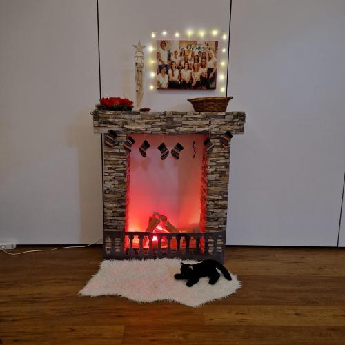 Ein Kamin steht vor der weißen Wand und eine Stoffkatze liegt vor ihm auf dem Fell