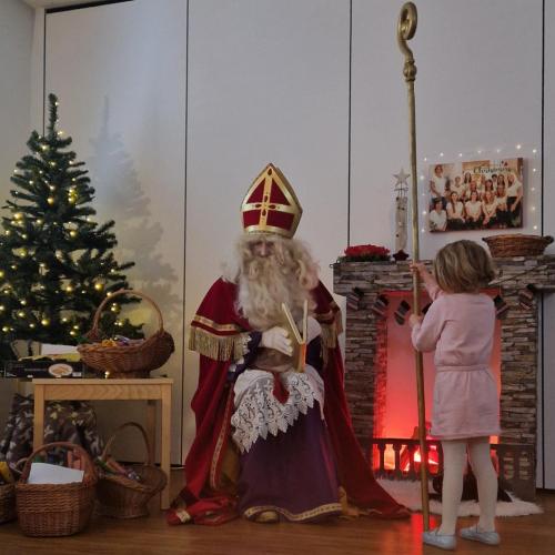 Der Nikolaus sitzt vor dem beleuchtenden Tannenbaum und ein Kind hält seinen Nikolausstab