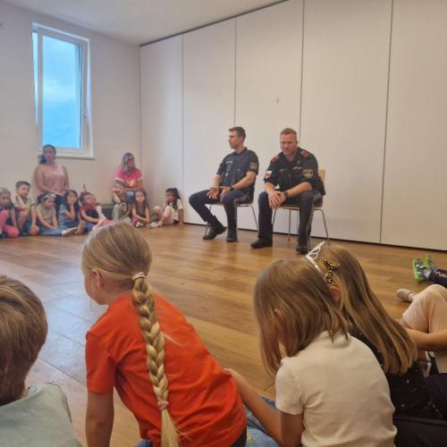 Die zwei Polizeibeamte sitzen in dem Bewegungsraum und erzählen den Kindern etwas über ihre Arbeit