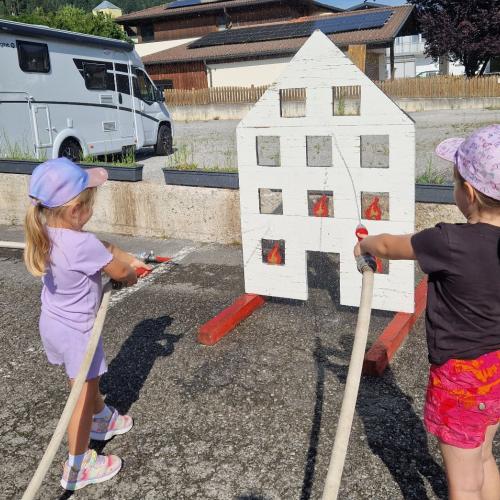 Zwei Kinder spritzen mit dem Feuerwehrschlauch das Feuer in den Fenstern eines Holzhauses um