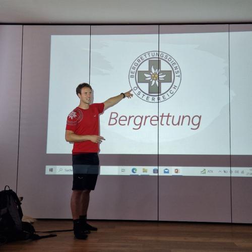Ein Mann der Bergrettung steht vor dem Beamerbild des Logos der Bergrettung