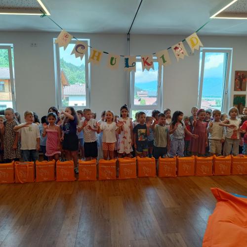 Die zu verabschiedenden Kinder stehen hinter ihren Abschlusstaschen und winken zum Abschlusslied