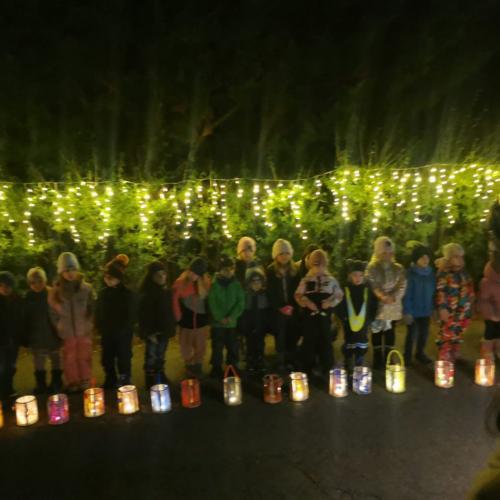 Die Kinder stehen im Dunklen vor einer leuchtenden Hecke und ihre Laterne stehen am Boden vor ihnen