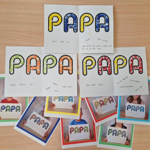 Die Vatertagskarten 2026, Auf der Vorderseite befindet sich ein Foto des Kindes das den verzierten "PAPA"-Schriftzug hält. Dieser Schriftzug befindet sich im Karteninneren und wurde mit Eigenschaften des Vaters vervollständigt