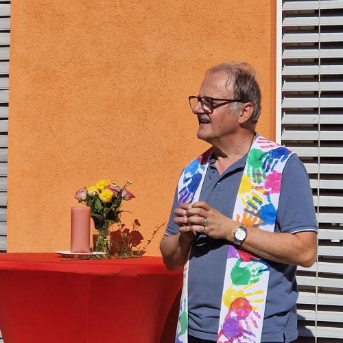 Pfarrer Josef mit seiner Stola steht neben einem mit Blumen und einer Kerze geschmücktem Stehtisch