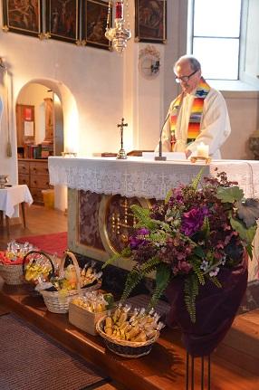 Der Herr Pfarrer steht hinter dem Altar und im Vordergrund sind die Körbe mit den Bienenwachskerzen zu sehen 