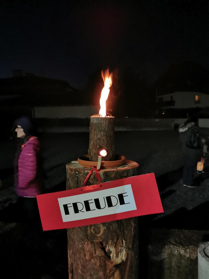 Eine brennende Baumkerze auf einen Baumstamm stehend, mit dem Schriftzug FREUDE 