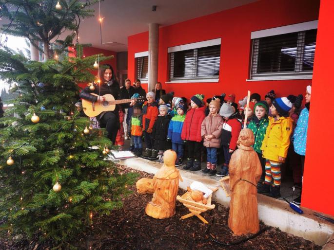 Singende Kinder vor dem Weihnachtsbaum und den großen Krippenfiguren