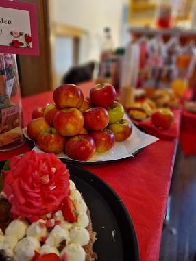 Eine Apfelpyramide mit einem "Freiwilligen Spenden Glas" und einer Torte mit Rose vom Buffet