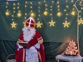 Der Nikolaus sitzt auf dem Stuhl und liest aus dem goldenen Buch. Im Hintergrund leuchten viele Sterne