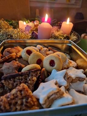 © cc Ein vollgefüllte Keksdose steht vor dem Adventkranz, an dem alle vier Kerzen brennen