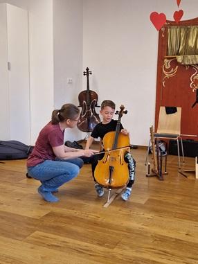 Ein Kind darf mit Hilfe der Musiklehrerin ein Kinderchello spielen