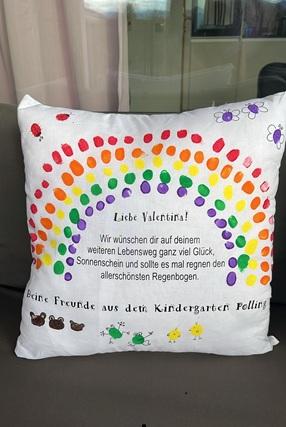 Ein Polster mit Fingerabdrücken der Kinder in Form eines Regenbogens und einem Text in der Mitte