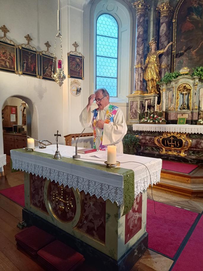 © cc Pfarrer Josef steht hinter dem Altar und macht beim Segen ein Kreuzzeichen auf seine Stirn.