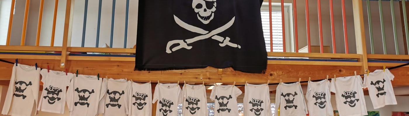 Eine Piratenflagge und viele T-Shirts mit Totenkopf hängen an einer Schnur