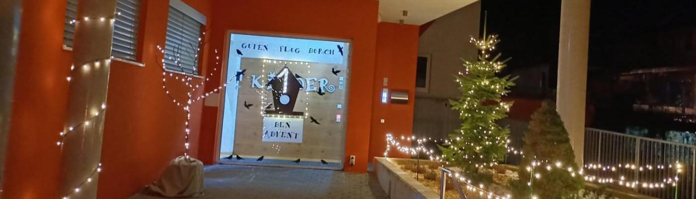 Der beleuchtete Vorplatz des Kindergartens mit dem gestalteten Adventfenster. " Guten Flug durch den Advent"