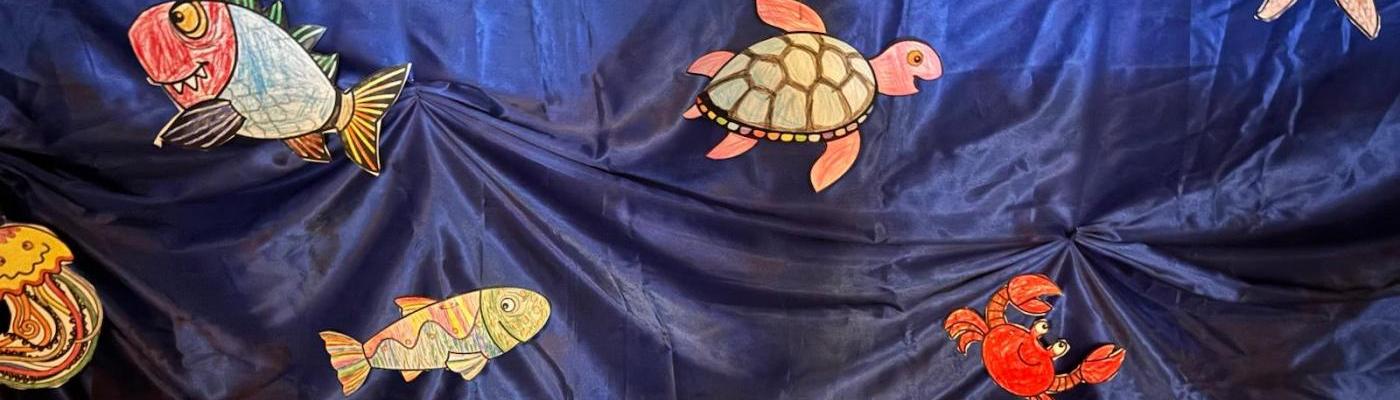 Von Kinder bemalte Wassertiere sind an einen blauem Seidentuch befestigt