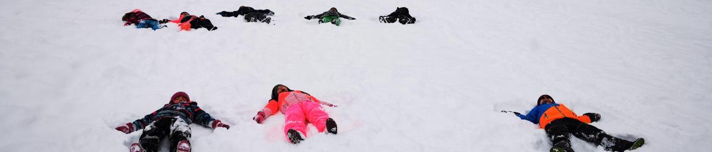 Kinder die im Schnee liegen und einen Schneeengel machen