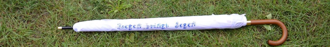 Ein weißer Regenschirm in einer Hülle mit dem Spruch: "Regen bringt Segen"