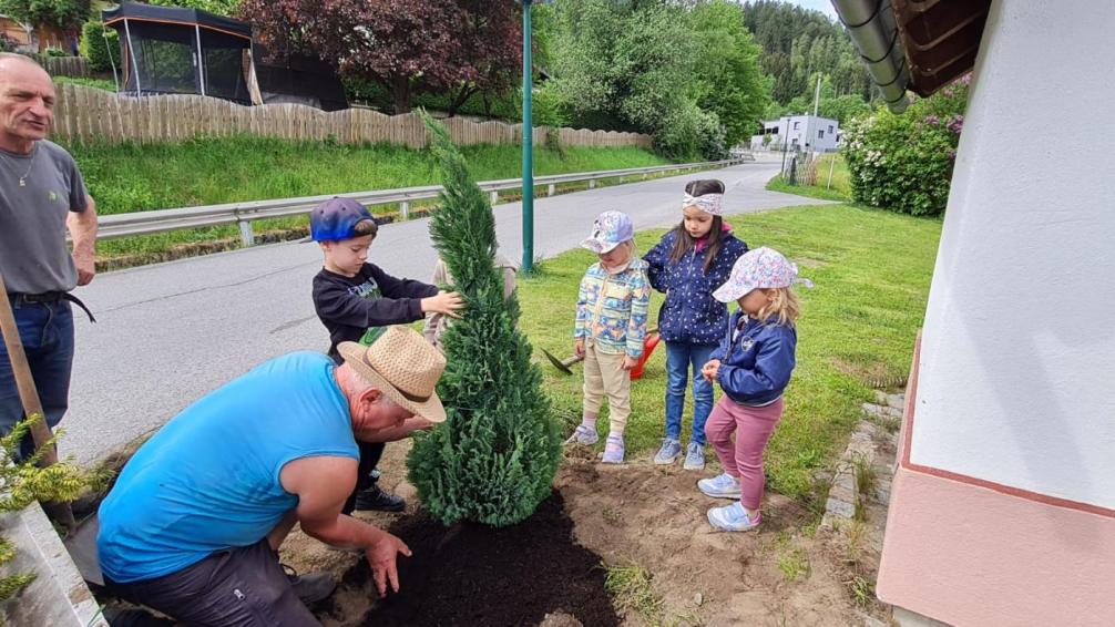 Der Landschaftsgärtner Albin setzt mit 4 Kindern einen Lebensbaum neben der Kapelle ein