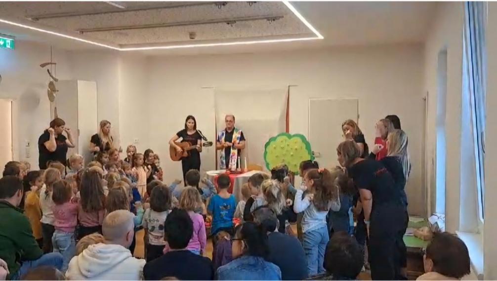 Alle Kinder und die Betreuer stehen um Pfarrer Josef uns singen ein Lied. Eltern beobachten das Geschehen