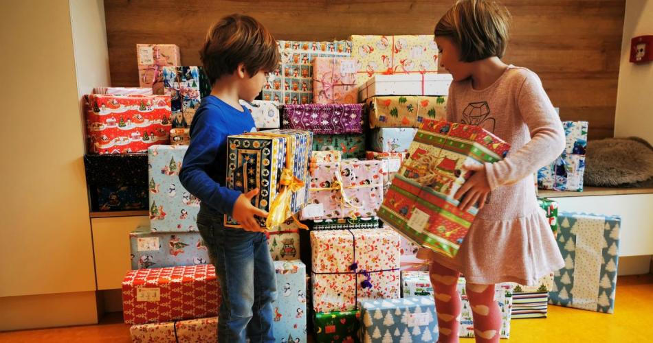 Zwei Kinder stellen ein Geschenk zu den vielen Anderen