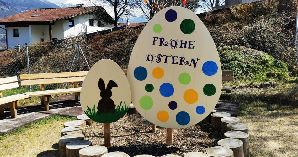 Große Holzeier die von den Kindern bemalt wurden stecken in der Erde im Garten des Kindergartens