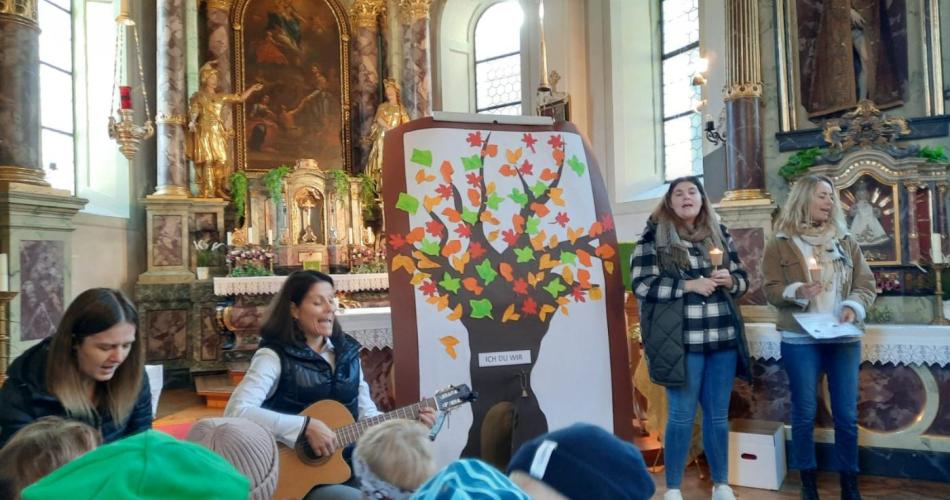 Vier Pädagogen singend vor dem Altar in der Kirche, mittig ein Bild von einem gebastelten Herbstbaum
