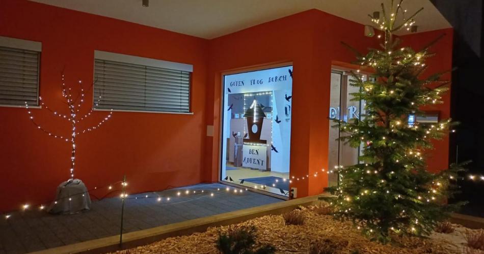 Der beleuchtete Vorplatz des Kindergartens mit dem gestalteten Adventfenster. " Guten Flug durch den Advent"
