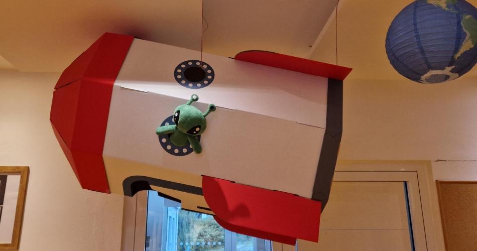 Eine hängende Karton-Rakete im Garderobenbereich aus deren Fenster ein Alien schaut