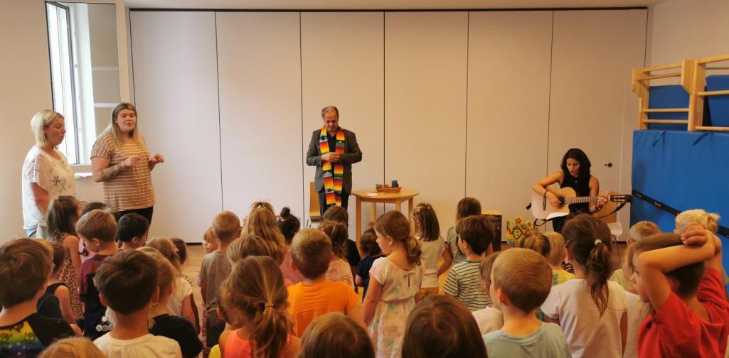 Verena Der Herr Pfarrer und drei Pädagoginnen mit vielen Kindern, die Bewegungen zu dem Lied machen