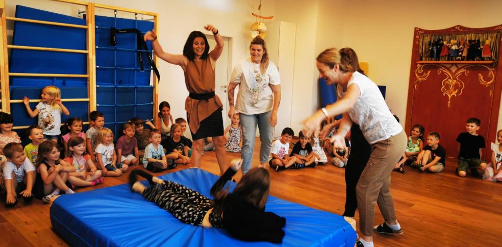 Verena Vier Erwachsene halten eine Frau an Händen und Füßen und werfen sie dann auf eine Matte