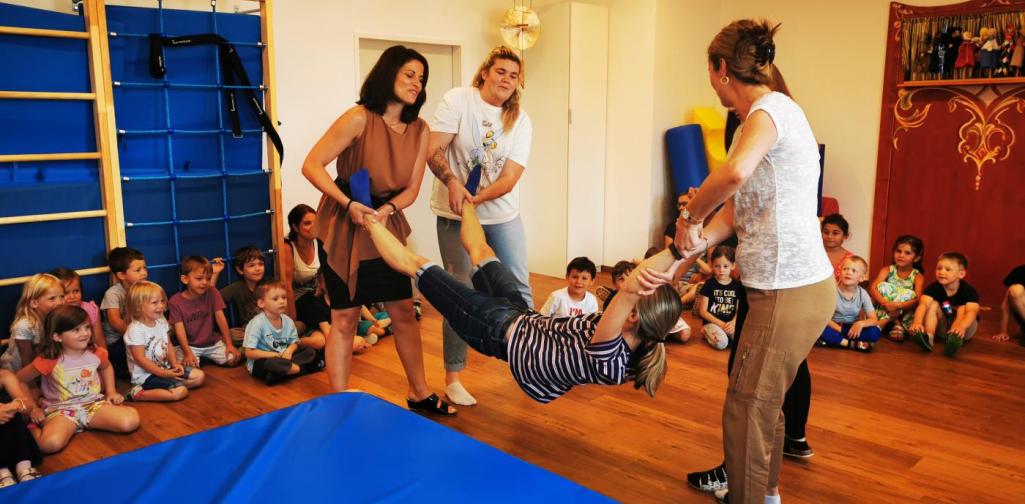 Verena Vier Erwachsene halten eine Frau an Händen und Füßen und schaukeln sie und werfen sie dann auf eine Matte