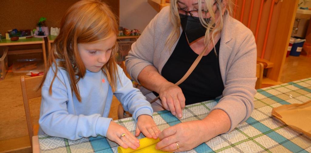 Ein Mädchen rollt die Bienenwachsplatte zur Kerze ein