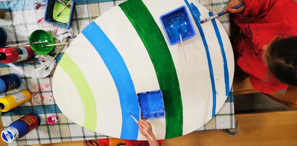 Verena Kinder bemalen das Holzei mit bunten Streifen