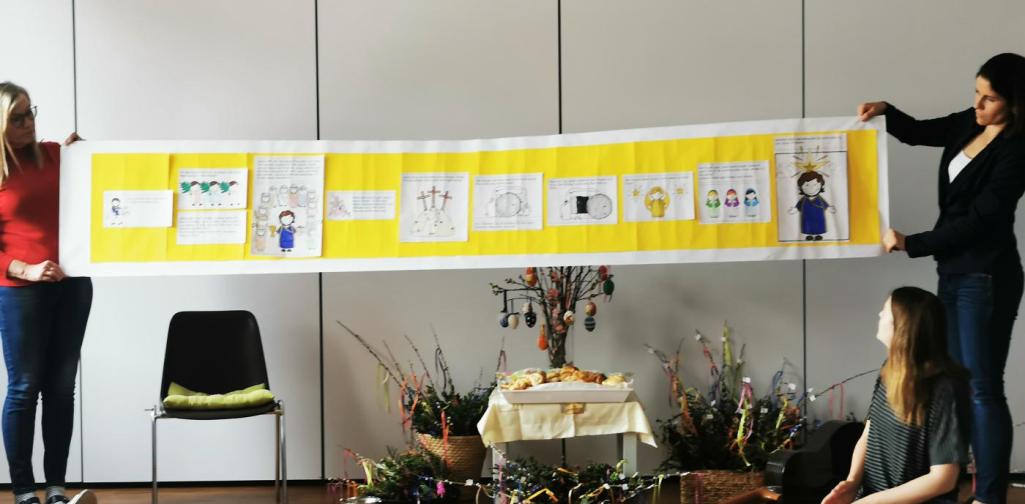 Verena Zwei Pädagoginnen halten eine Bilderrolle mit der Ostergeschichte