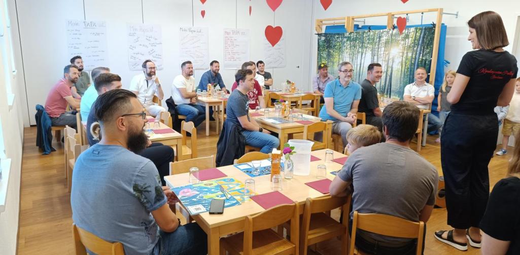 Verena Eder Kindergartenpädagogin begrüßt Väter, die am gedeckten Frühstückstisch sitzen