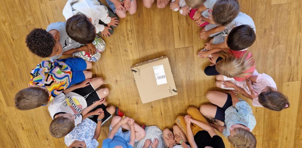 Verena Eder unsere ältesten Kinder sitzen im Kreis. In der Mitte liegt das Paket, welches wir im Personalshop bepackt und versendet haben