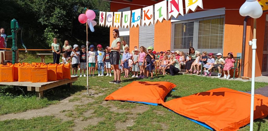Verena Eder Die Kindergartenleiterin Barbara mit allen Kindern die in die Schule kommen. Sie stehen im Garten neben den großen Polstern unter der "Schulkind-girlande"