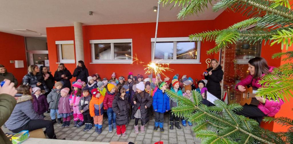 Verena Eder Die Kinder stehen um den Tannenbaum vor dem Kindergarten und singen während ein Sternspritzer leuchtet