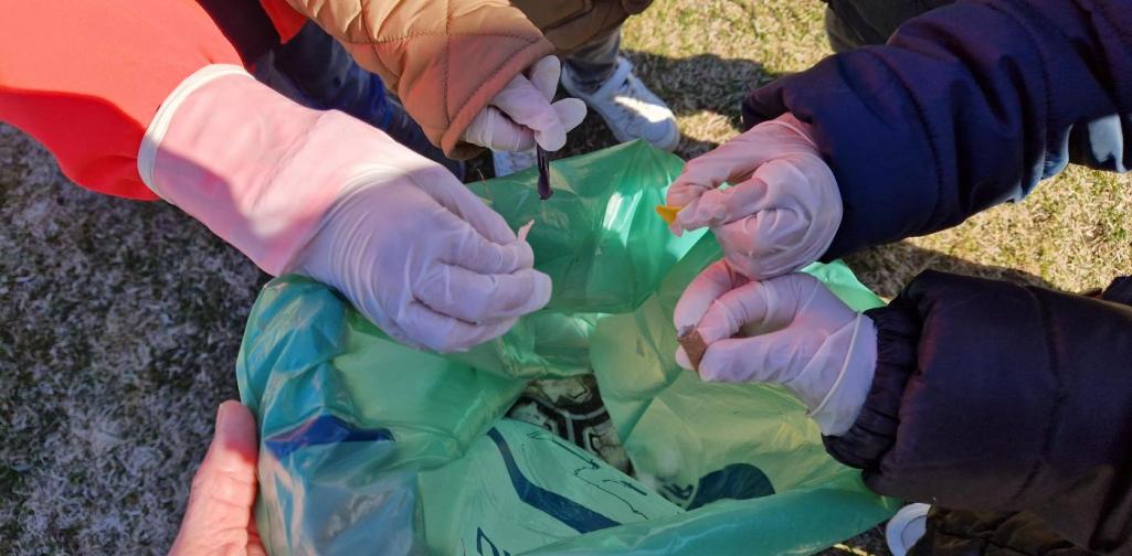 Verena Eder Vier Kinderhände haben Handschuhe an und wollen Müll in den Müllsack werfen