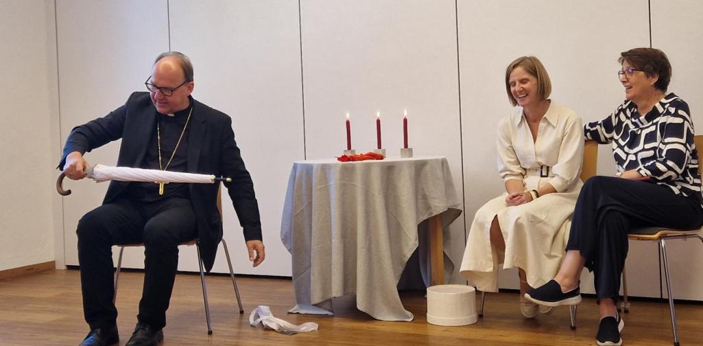 Verena Eder Der Bischof Herman Glettler packt den Schirm aus seiner Verpackung aus, Frau Rothbacher und Pastoralass. schauen zu Christine