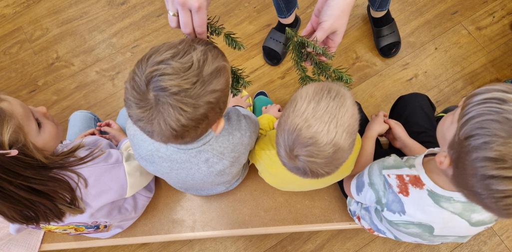 Verena Eder Von oben fotografiert sieht man zwei Kinder, die an einem Tannenzweig riechen