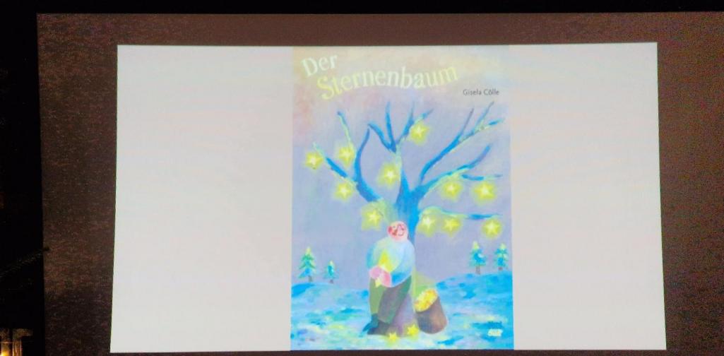 Verena Eder Das Bilderbuchcover von "Der Sternenbaum" auf einer Leinwand im Dunkeln
